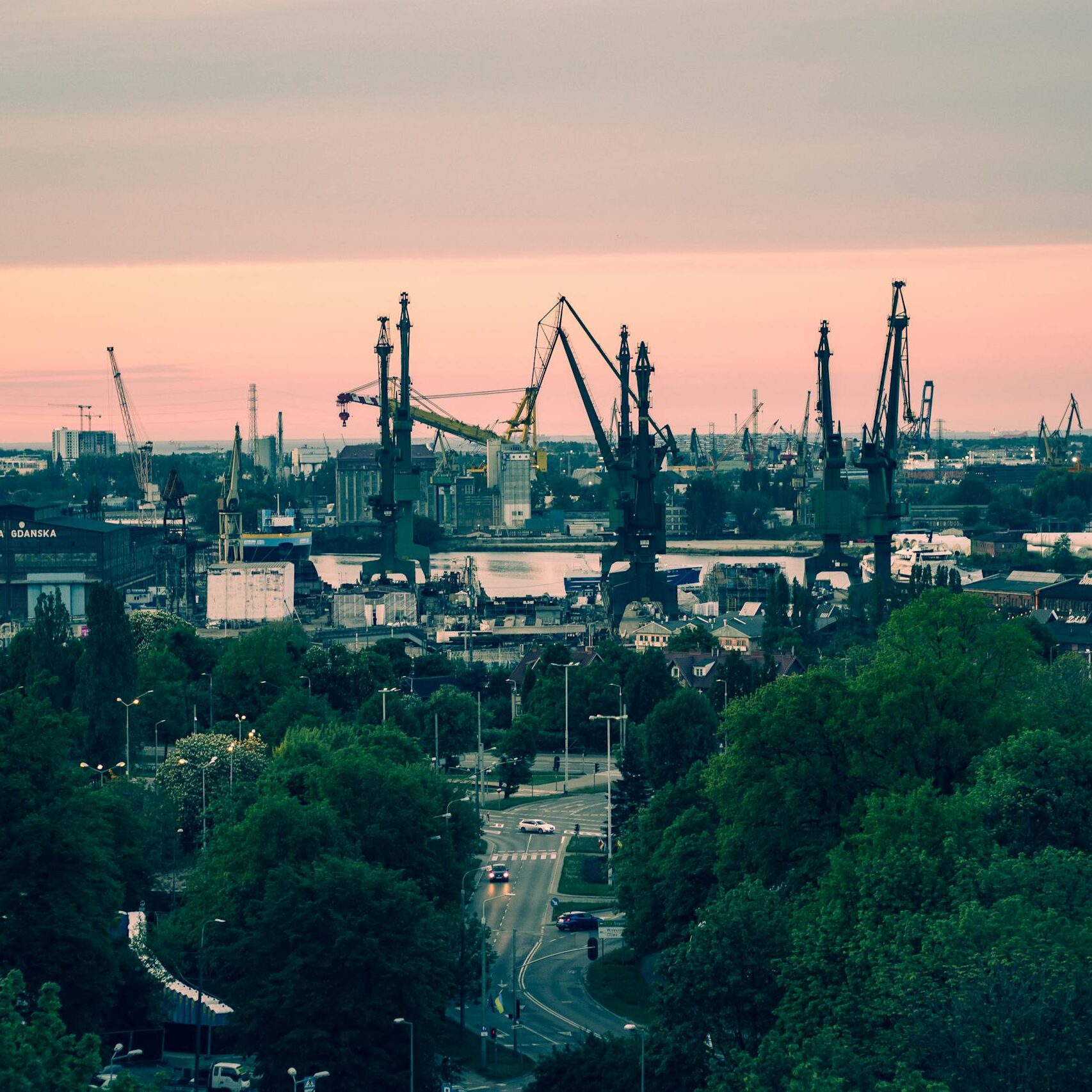 A panoramic view of the iconic Gdańsk shipyard with cranes silhouetted against a vibrant sunset sky.